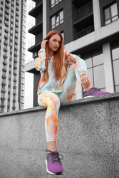 Beautiful woman in gym clothes sitting on parapet on street, low angle view