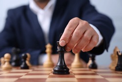 Man with king game piece playing chess at checkerboard, closeup