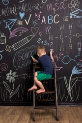 three-year-old boy draws with multi-colored chalk on a large blackboard. black wall with children's drawings and formulas. vertical photography.