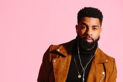 Cool young African American man with beard looking at camera, isolated on pink studio background
