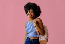 attractive girl in eyeglasses with backpack posing on pink background, back to school concept