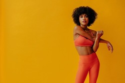 attractive young fit woman in sportswear stretching isolated on orange background 