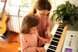 Woman and girl playing a piano. Beautiful mom teaching her daughter playing a piano..	