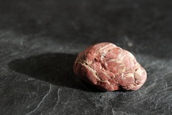 Uncut and raw brownish-red jasper stone, on gray slate background, lit by the sun