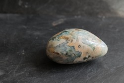 Blue-green orbicular jasper tumbled pebble, on gray slate background