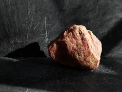 Uncut and raw rhodochrosite stone, on gray slate background, lit by the sun  