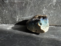 Uncut and raw, opaque blue obsidian, on gray slate background, lit by the sun 