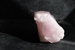 Uncut and raw rose quartz stone on gray slate background, lit by the sun