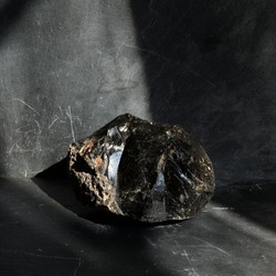 Uncut, unprocessed black obsidian, on gray slate background, lit by the sun