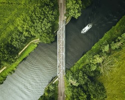 Aerial view of a train bridge crossing a river with a white boat at sunset or dawn in germany shot with a drone. Birdseye view of river with a boat.