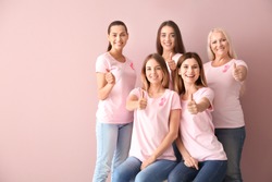 Beautiful women of different ages with pink ribbons showing thumbs-up gesture on color background. Breast cancer concept