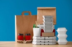 Different packages and carton cups on table against color background. Food delivery service