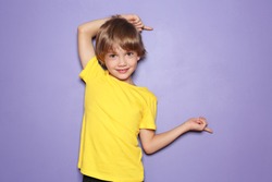Little boy in t-shirt pointing at something on color background