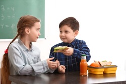 Little boy sharing his school lunch with girl in classroom