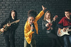 Band of teenage musicians playing against dark wall