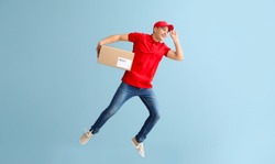 Jumping young male courier with box on grey background