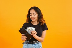 Asian woman putting money into wallet on color background