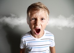 Portrait of angry little boy with steam coming out of ears on grey background