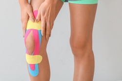 Sporty woman with physio tape applied on knee against light background, closeup