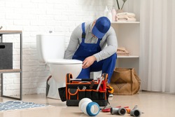 Handsome plumber repairing toilet bowl in bathroom