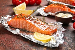 Foil with cooked salmon fillet on color background