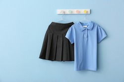 Stylish school uniform hanging on color wall
