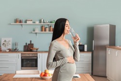Beautiful pregnant woman drinking water in kitchen