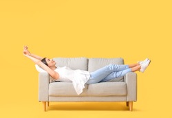 Young woman relaxing on sofa against color background