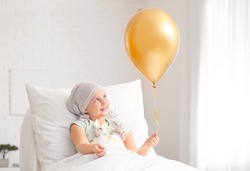 Little girl with golden balloon undergoing course of chemotherapy in clinic. Childhood cancer awareness concept