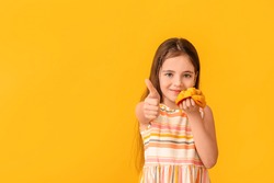 Cute little girl with fresh mango showing thumb-up gesture on color background