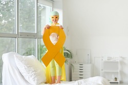Little girl with golden ribbon wearing superhero costume in clinic. Childhood cancer awareness concept