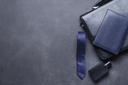 Stylish necktie with briefcase, perfume bottle and notebook on dark background