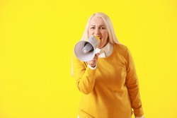 Screaming mature woman with megaphone on color background