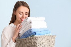 Young woman with clean laundry on light background