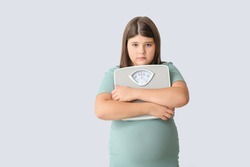 Sad overweight girl with measuring scales on light background