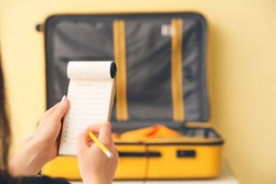 Woman making check-list of things to pack for travel at home