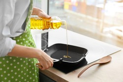 Woman pouring sunflower oil onto frying pan in kitchen