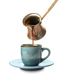 Pouring hot coffee from cezve into cup on white background