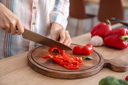 Woman cutting bell pepper in kitchen, closeup