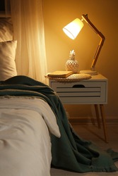 Big comfortable bed and table with glowing lamp in room at night
