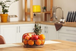 Basket with fresh fruits on wooden table in kitchen
