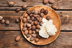 Plate with shea butter and nuts on wooden background