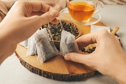Woman with tea bags and dry leaves on light background