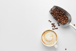 Cup of hot cappuccino and scoop with coffee beans on white background