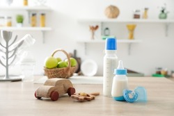 Bottles of milk for baby with toys on table in kitchen