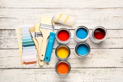 Cans of paints with palette samples, brushes and roller on light wooden background