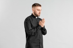 Young priest praying to God on light background