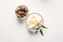 Bowls with shea butter and nuts on light background