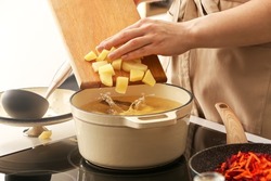 Woman adding potato to cooking pot in kitchen