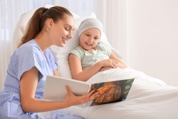 Woman reading book to her daughter who is undergoing course of chemotherapy in clinic. Childhood cancer awareness concept